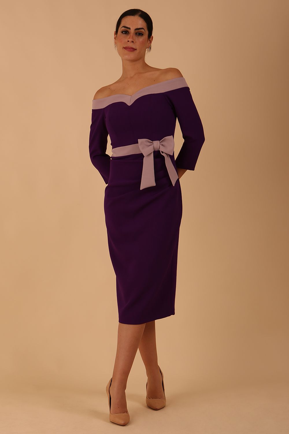 Model wearing a diva catwalk Brittany Off Shoulder Bow detail Pencil Dress with 3/4 sleeves and knee length in Deep Purple and Thunder Bird colour