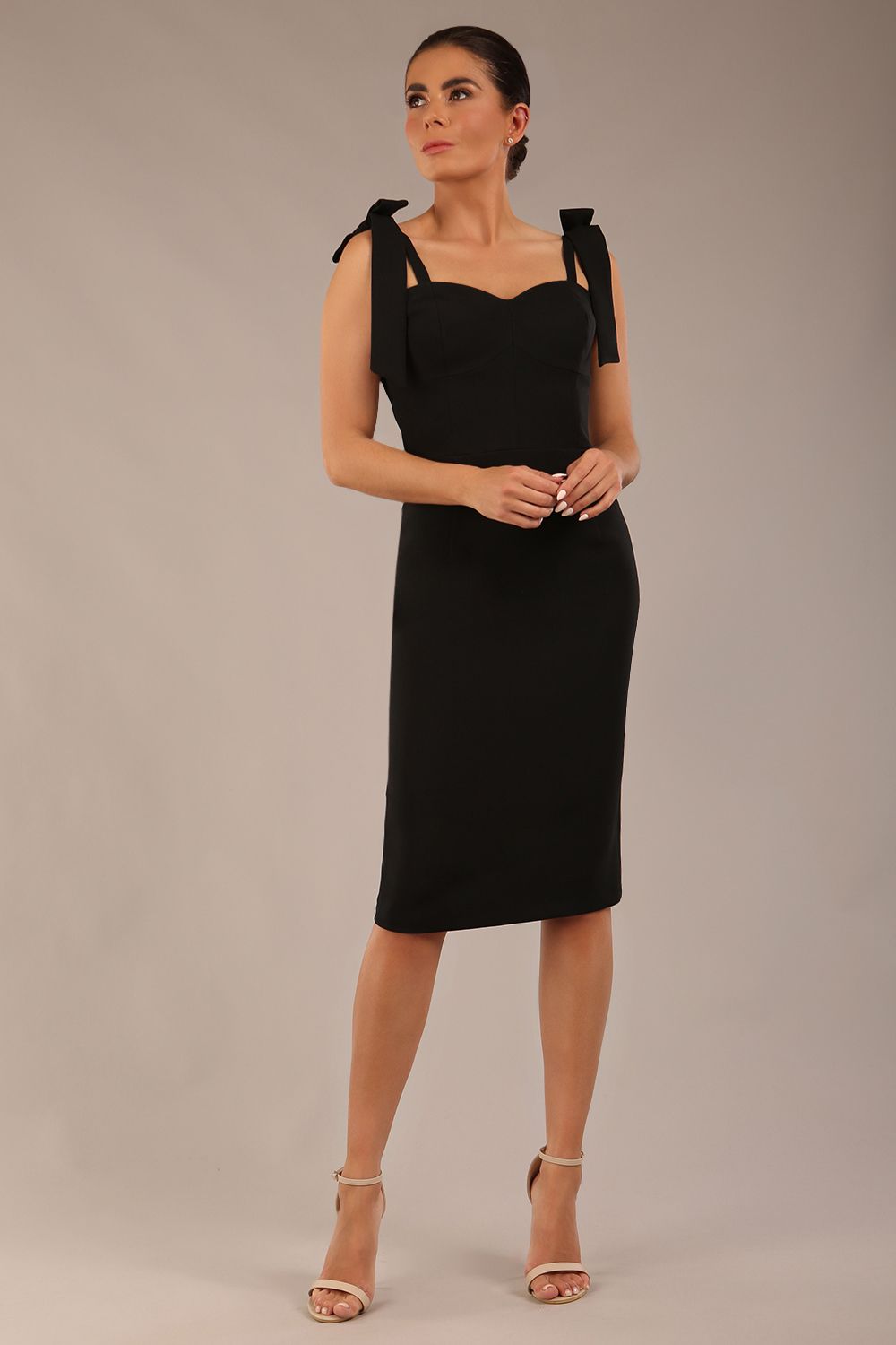 brunette model wearing a diva catwalk Philippa Pencil Wiggle Dress sleeveless style, tie detail on the shoulders knee length and sweetheart neckline in black colour front 