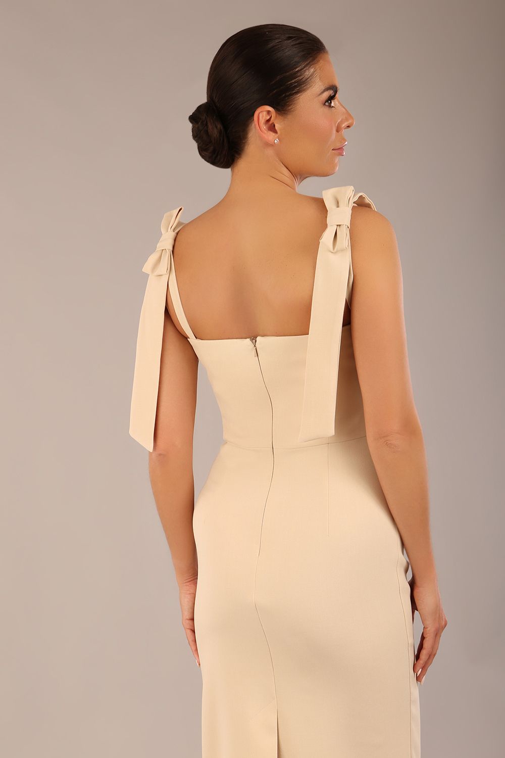 brunette model wearing a diva catwalk Philippa Pencil Wiggle Dress sleeveless style, tie detail on the shoulders knee length and sweetheart neckline in sandshell beige back