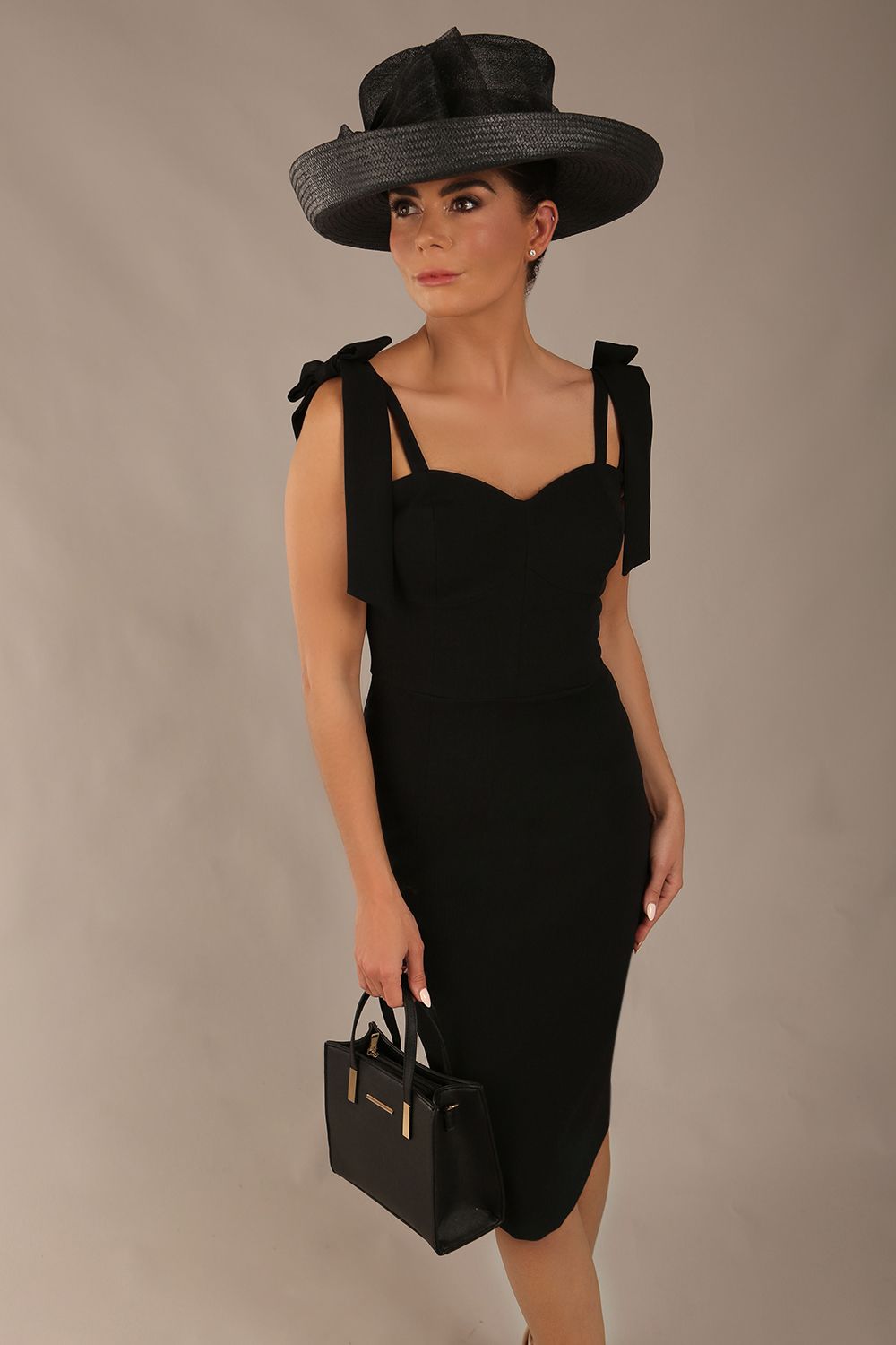 brunette model wearing a diva catwalk Philippa Pencil Wiggle Dress sleeveless style, tie detail on the shoulders knee length and sweetheart neckline in black colour front with hat