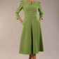 A model wearing a red, 3/4 sleeve A-line dress with pockets, featuring a boat neckline and vent at the centre back (Citrus Green)