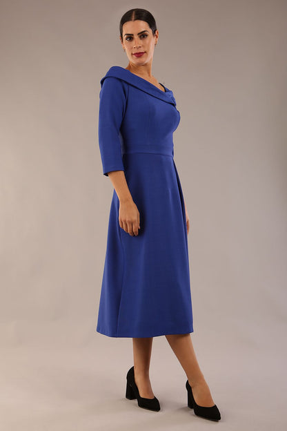 A model wearing a diva catwalk SEED Chrysanta sculptural collar dress 3/4 sleeve A-line dress with a round neckline and concealed zip at the back (Monaco Blue)
