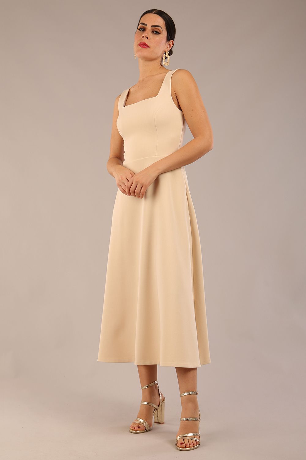 brunette model is wearing a diva catwalk Tamsin Square Neckline Swing Dress sleeveless style with a midaxi  length and side pockets in sandshell beige colour front
