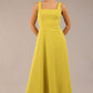 brunette model is wearing a diva catwalk Tamsin Square Neckline Swing Dress sleeveless style with a midaxi  length and side pockets in Citrus green colour front