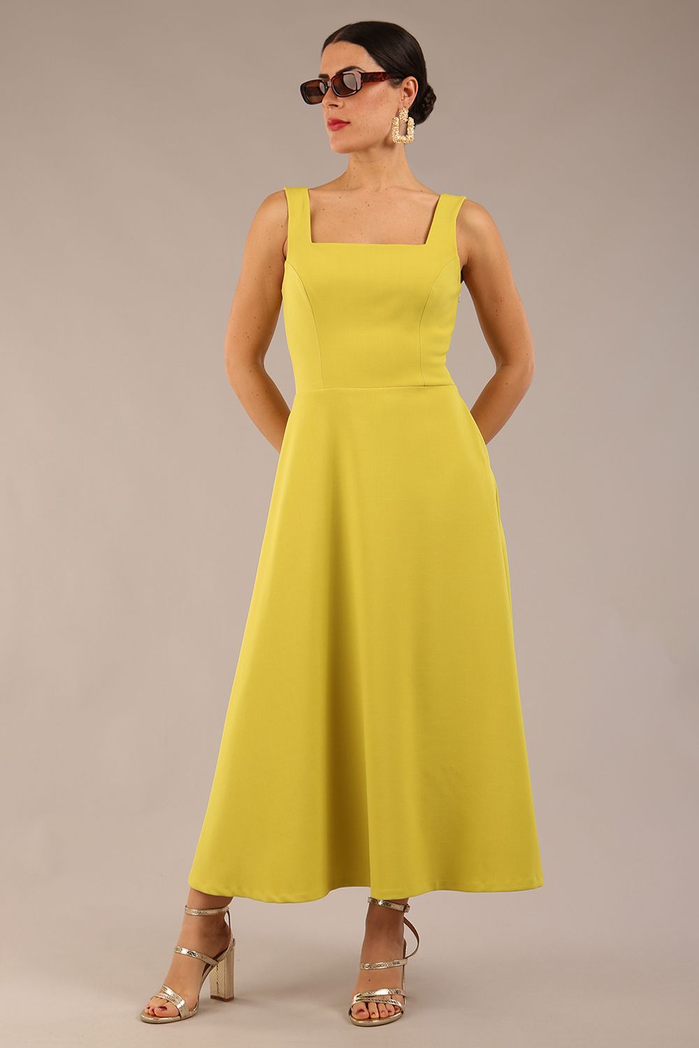 brunette model is wearing a diva catwalk Tamsin Square Neckline Swing Dress sleeveless style with a midaxi  length and side pockets in Citrus green colour front