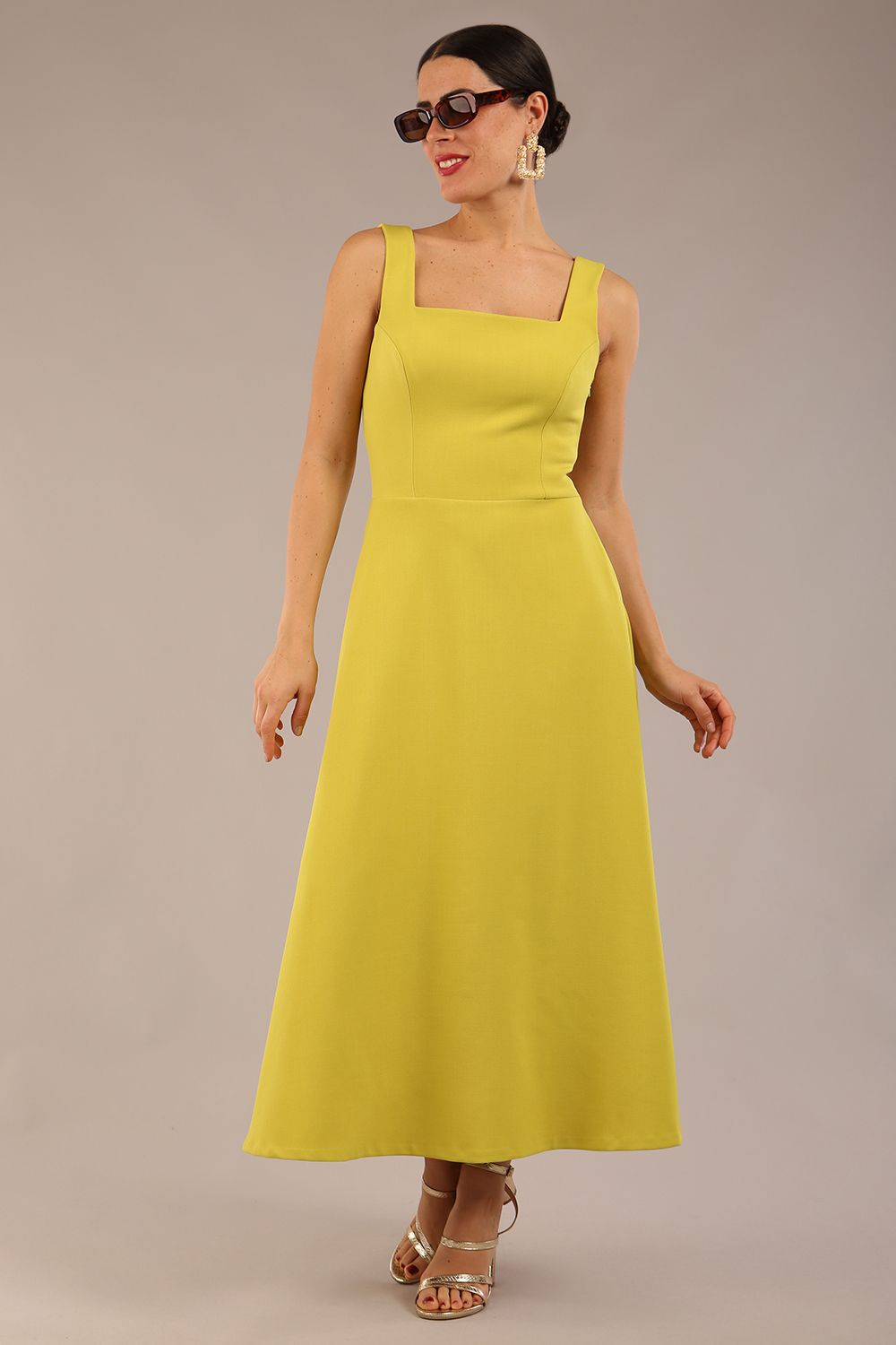 brunette model is wearing a diva catwalk Tamsin Square Neckline Swing Dress sleeveless style with a midaxi  length and side pockets in Citrus green colour front