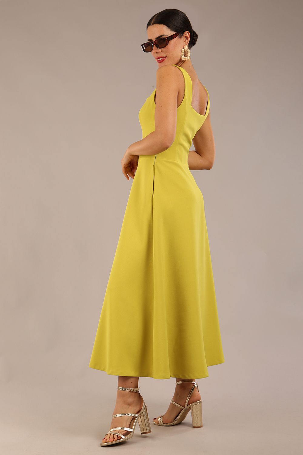 brunette model is wearing a diva catwalk Tamsin Square Neckline Swing Dress sleeveless style with a midaxi  length and side pockets in Citrus green colour back side