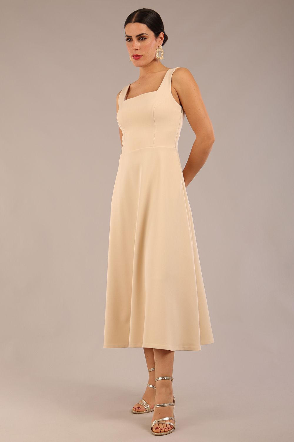 brunette model is wearing a diva catwalk Tamsin Square Neckline Swing Dress sleeveless style with a midaxi  length and side pockets in sandshell beige colour front