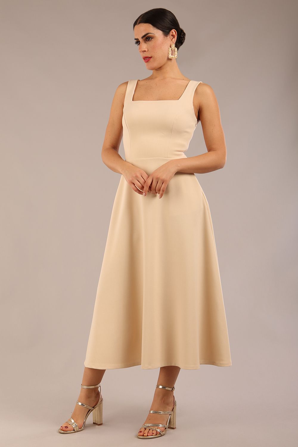 brunette model is wearing a diva catwalk Tamsin Square Neckline Swing Dress sleeveless style with a midaxi  length and side pockets in sandshell beige colour front