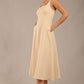 brunette model is wearing a diva catwalk Tamsin Square Neckline Swing Dress sleeveless style with a midaxi  length and side pockets in sandshell beige colour front side