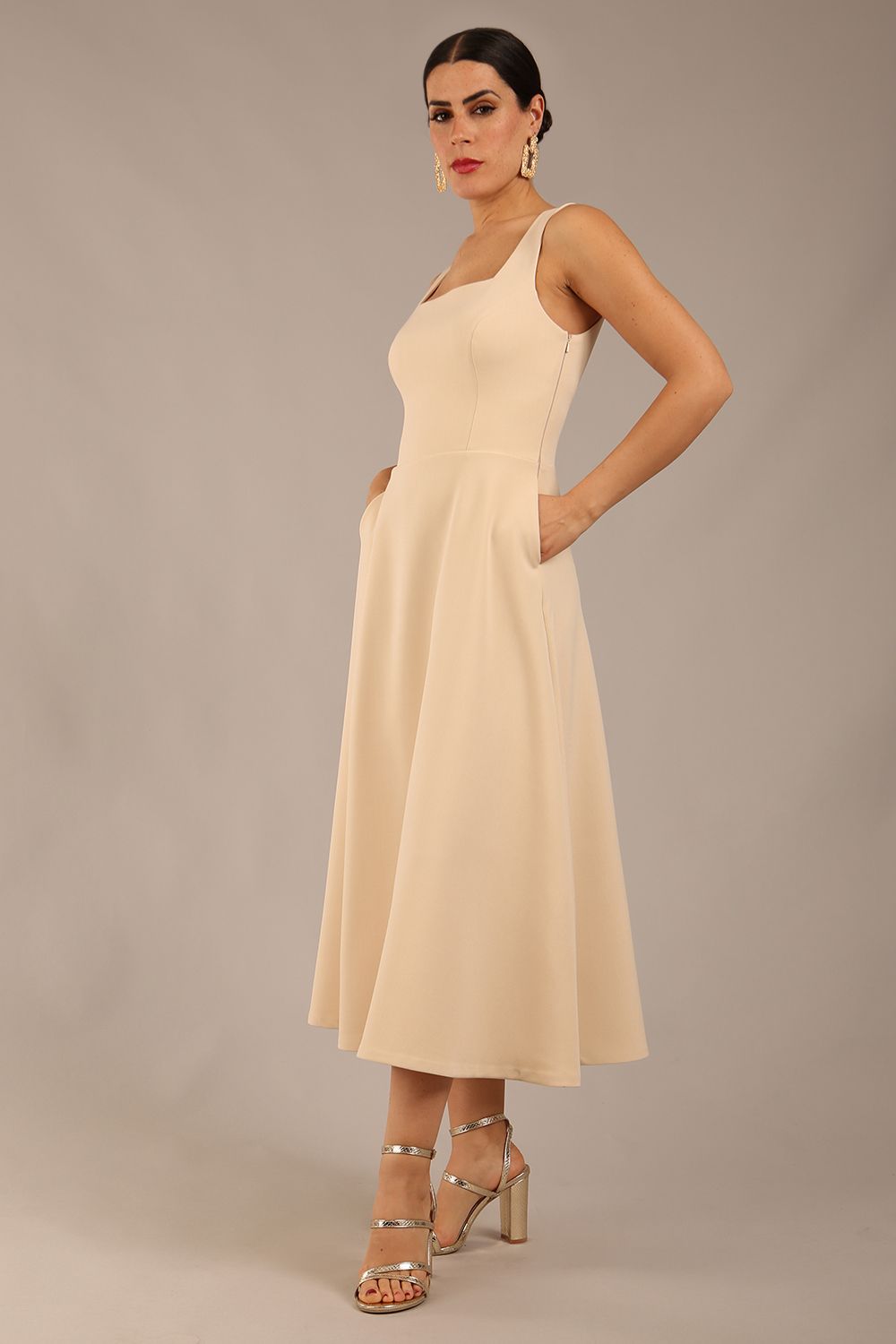 brunette model is wearing a diva catwalk Tamsin Square Neckline Swing Dress sleeveless style with a midaxi  length and side pockets in sandshell beige colour front side
