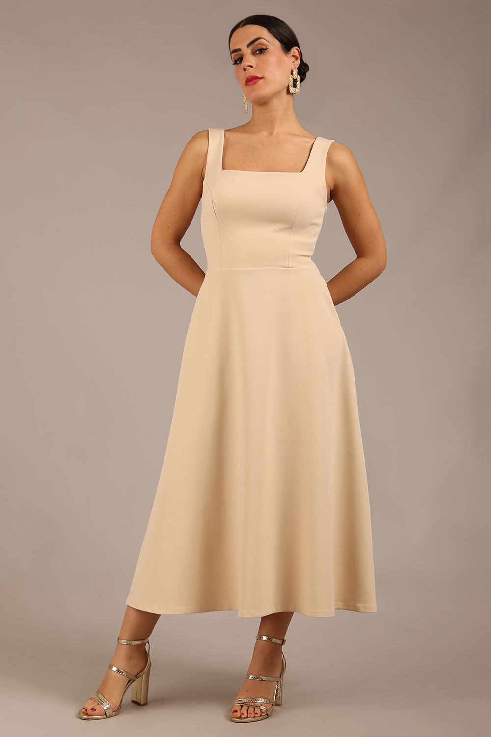 brunette model is wearing a diva catwalk Tamsin Square Neckline Swing Dress sleeveless style with a midaxi  length and side pockets in sandshell beige colour front