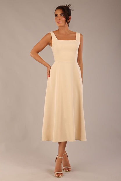 brunette model wearing a diva catwalk Tamsin Square Neckline Swing Dress sleeveless style with a midaxi  length and side pockets in Sandshell Beige colour front
