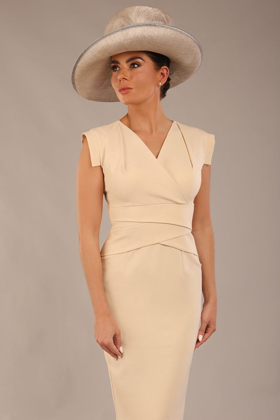 brunette model is wearing a diva catwalk Caprice Cap Sleeved Pencil Dress cap sleeve v neckline knee length with pleating details in sandshell beige colour front image with a hat