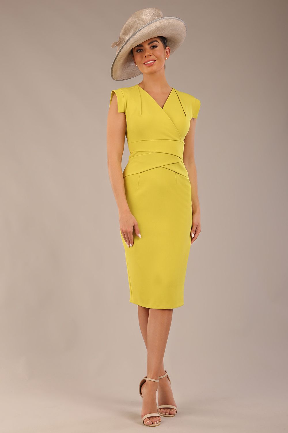 brunette model is wearing a diva catwalk Caprice Cap Sleeved Pencil Dress cap sleeve v neckline knee length with pleating details in citrus green colour front image with a hat