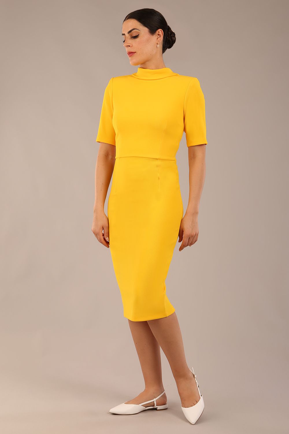 brunette model is wearing a diva catwalk Highmoor Short Sleeved Pencil Dress high neckline and shoulders pad in sunshine yellow colour front image