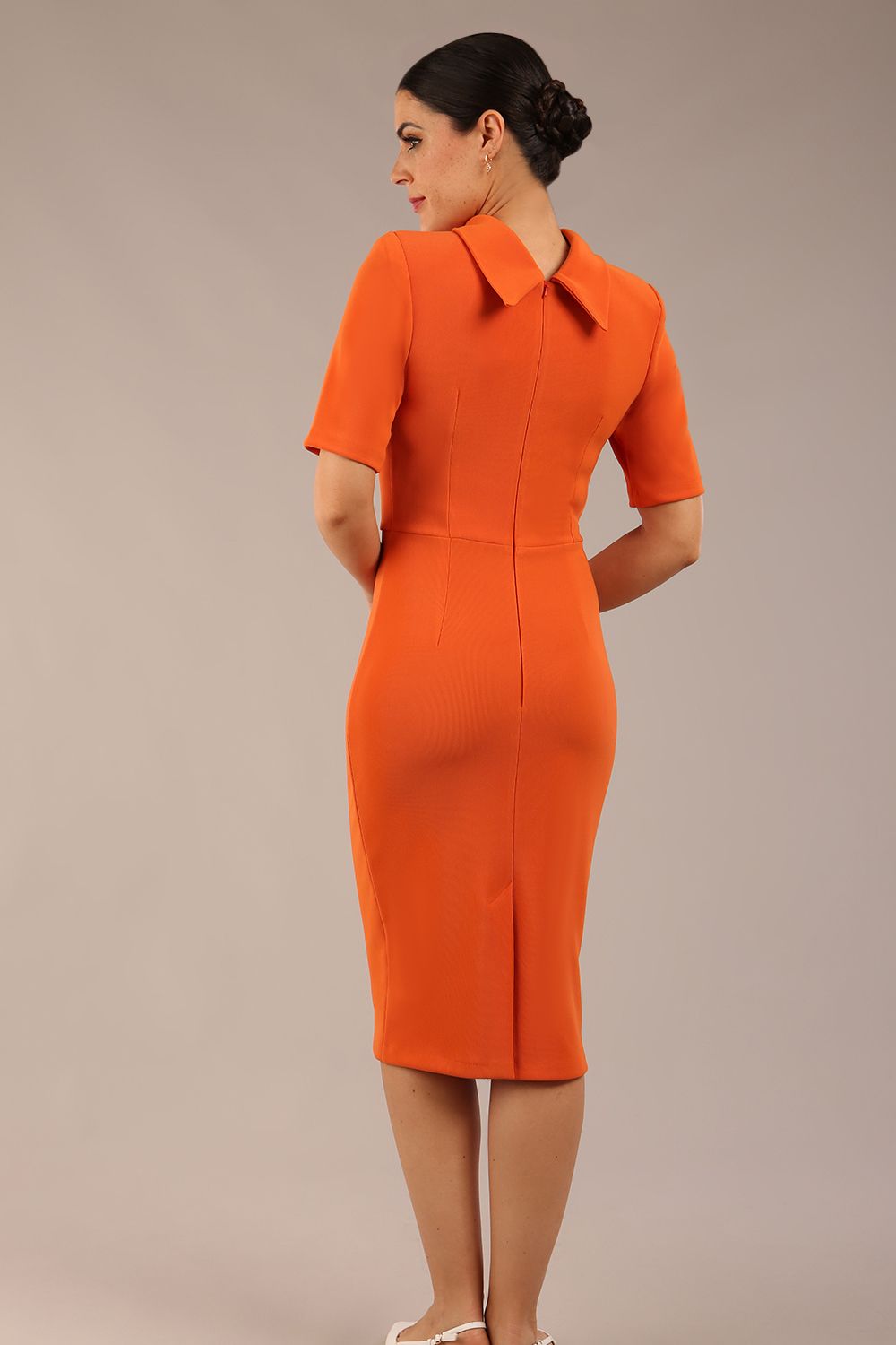 brunette model is wearing a diva catwalk Highmoor Short Sleeved Pencil Dress high neckline and shoulders pad in amber orange colour back image