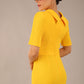 brunette model is wearing a diva catwalk Highmoor Short Sleeved Pencil Dress high neckline and shoulders pad in sunshine yellow colour back image