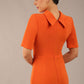 brunette model is wearing a diva catwalk Highmoor Short Sleeved Pencil Dress high neckline and shoulders pad in amber orange colour back image