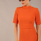 brunette model is wearing a diva catwalk Highmoor Short Sleeved Pencil Dress high neckline and shoulders pad in amber orange colour front image