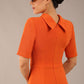 brunette model is wearing a diva catwalk Highmoor Short Sleeved Pencil Dress high neckline and shoulders pad in amber orange colour back image