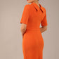 brunette model is wearing a diva catwalk Highmoor Short Sleeved Pencil Dress high neckline and shoulders pad in amber orange colour back image