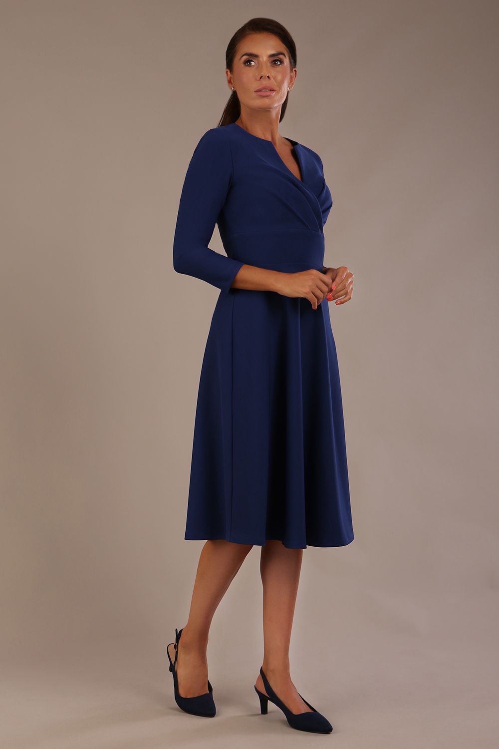brunette model is wearing a diva catwalk Haddington sleeved A-line Dress knee length round neckline with crossover v-slit detail in navy blue colour front side image
