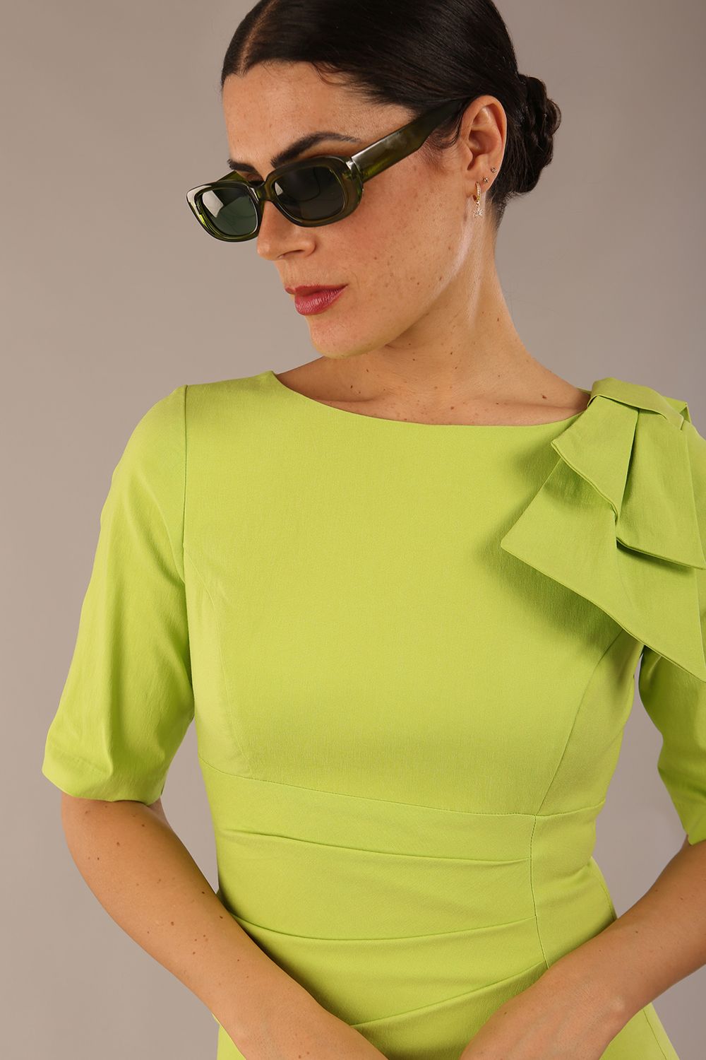 brunette model is wearing a diva catwalk Reverie Short Sleeve Stretch Pencil Dress with Bow Detail in lime green colour front image close up with sunglasses