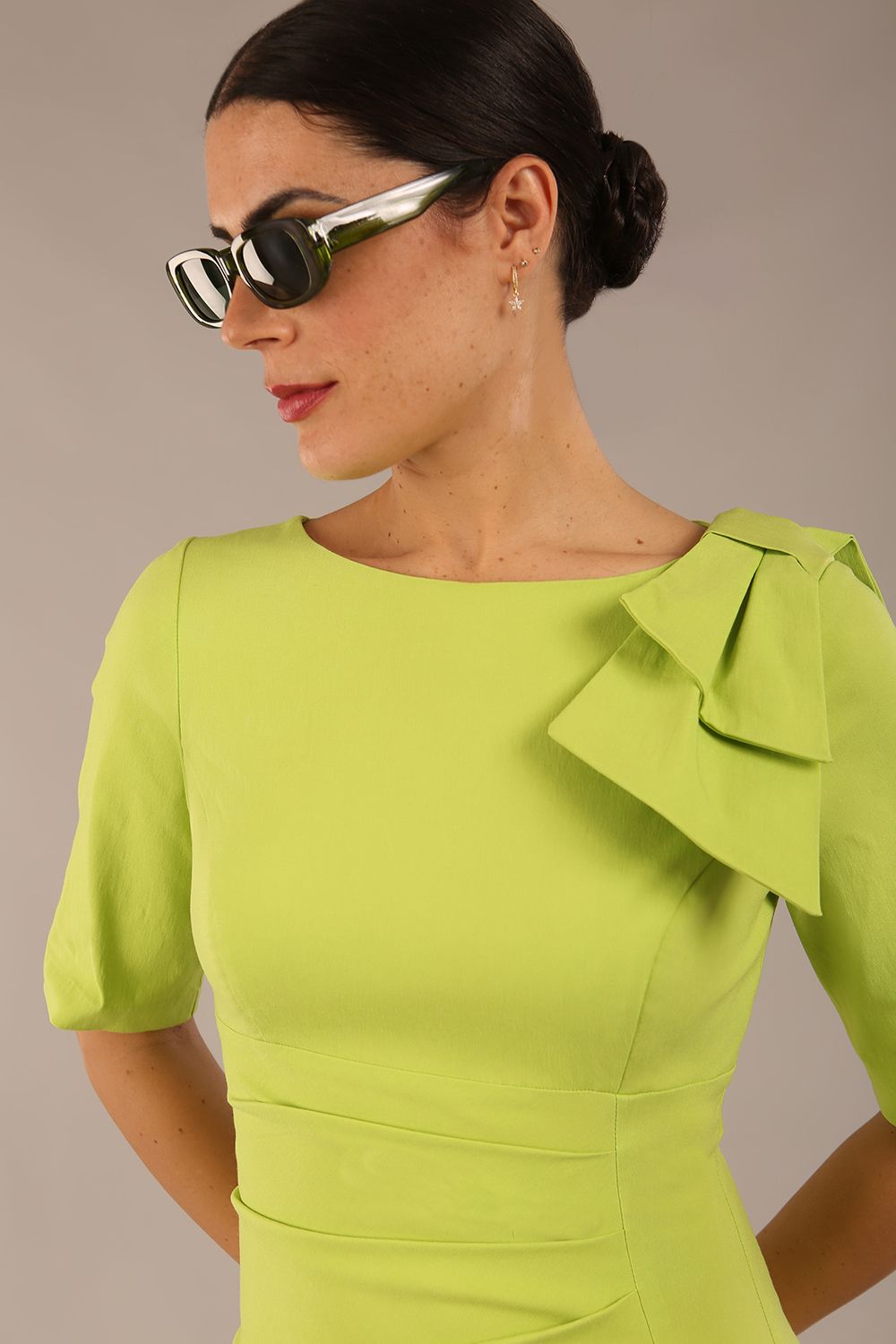 brunette model is wearing a diva catwalk Reverie Short Sleeve Stretch Pencil Dress with Bow Detail in lime green colour front image close up with sunglasses