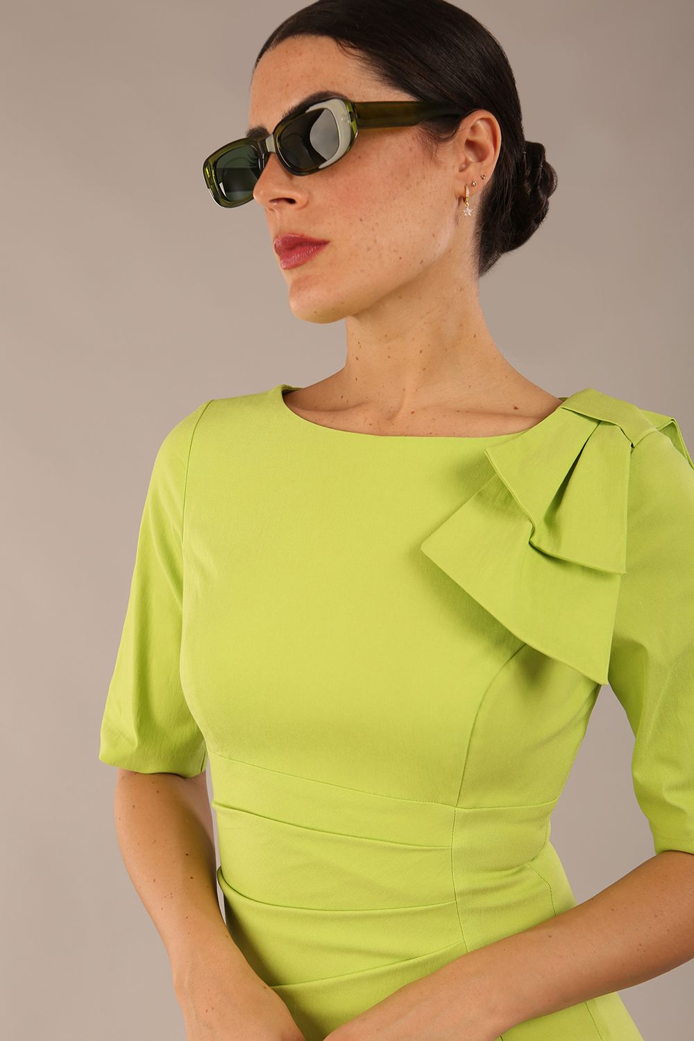 brunette model is wearing a diva catwalk Reverie Short Sleeve Stretch Pencil Dress with Bow Detail in lime green colour front image with sunglasses