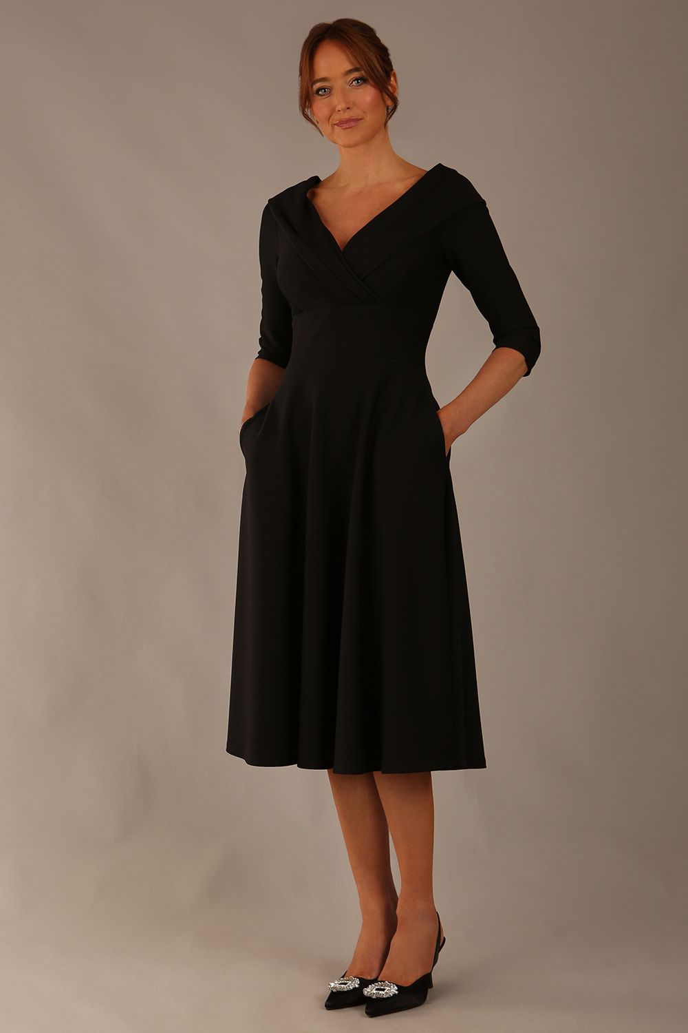 brunette model is wearing a diva catwalk Fabienne sleeved A-line Dress with pockets v neckline knee length wide waistband fold over v neckline in black colour front image