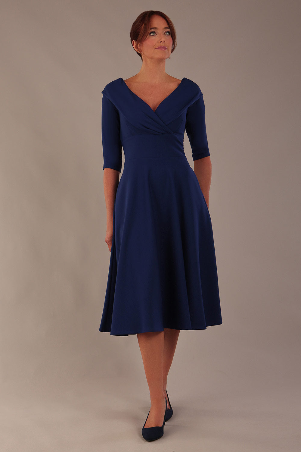 brunette model is wearing a diva catwalk Fabienne sleeved A-line Dress with pockets v neckline knee length wide waistband fold over v neckline in navy blue colour front image