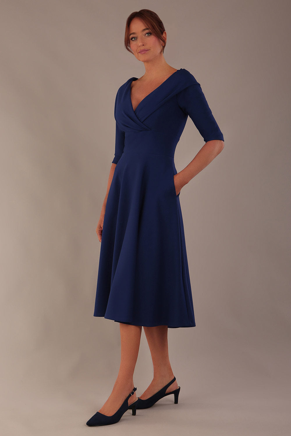 brunette model is wearing a diva catwalk Fabienne sleeved A-line Dress with pockets v neckline knee length wide waistband fold over v neckline in navy blue colour front image