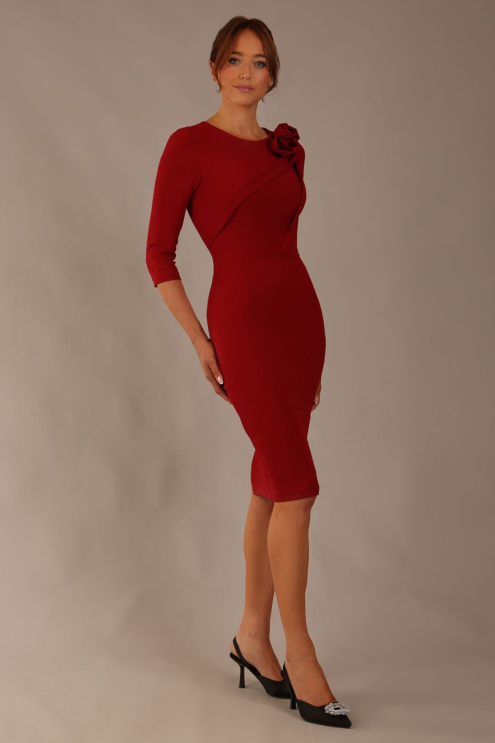 brunette model is wearing a diva catwalk Mirabelle ¾ Sleeves & Floral Shoulder Detail Pencil Dress with diagonal pleating across the front knee length in rosewood red colour front image