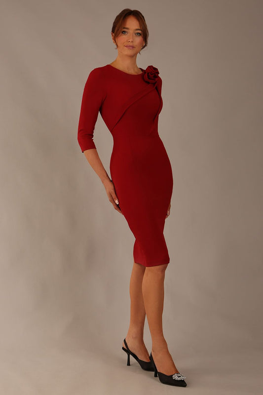 brunette model is wearing a diva catwalk Mirabelle ¾ Sleeves & Floral Shoulder Detail Pencil Dress with diagonal pleating across the front knee length in rosewood red colour front image
