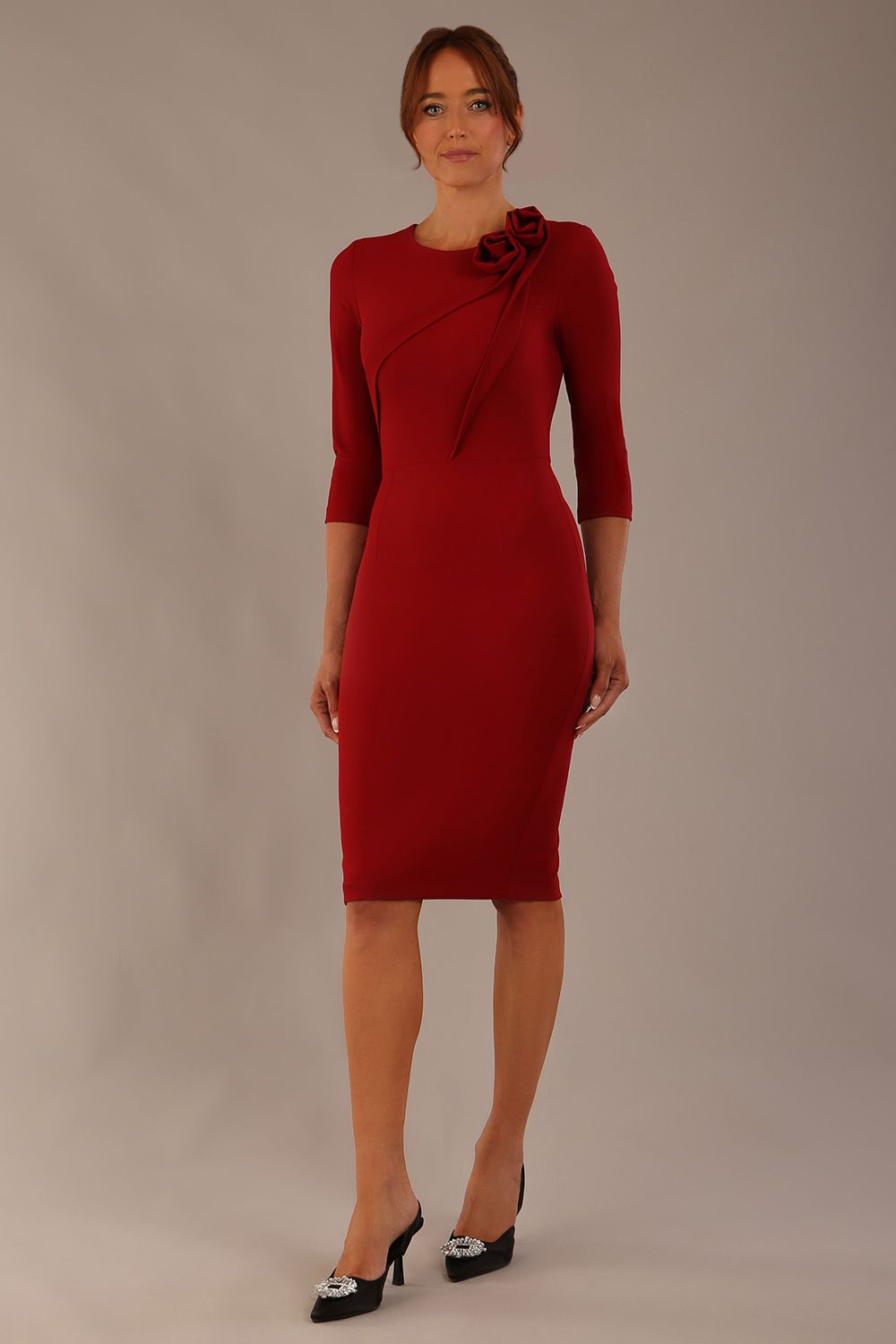 brunette model is wearing a diva catwalk Mirabelle ¾ Sleeves & Floral Shoulder Detail Pencil Dress with diagonal pleating across the front knee length in rosewood red colour front image