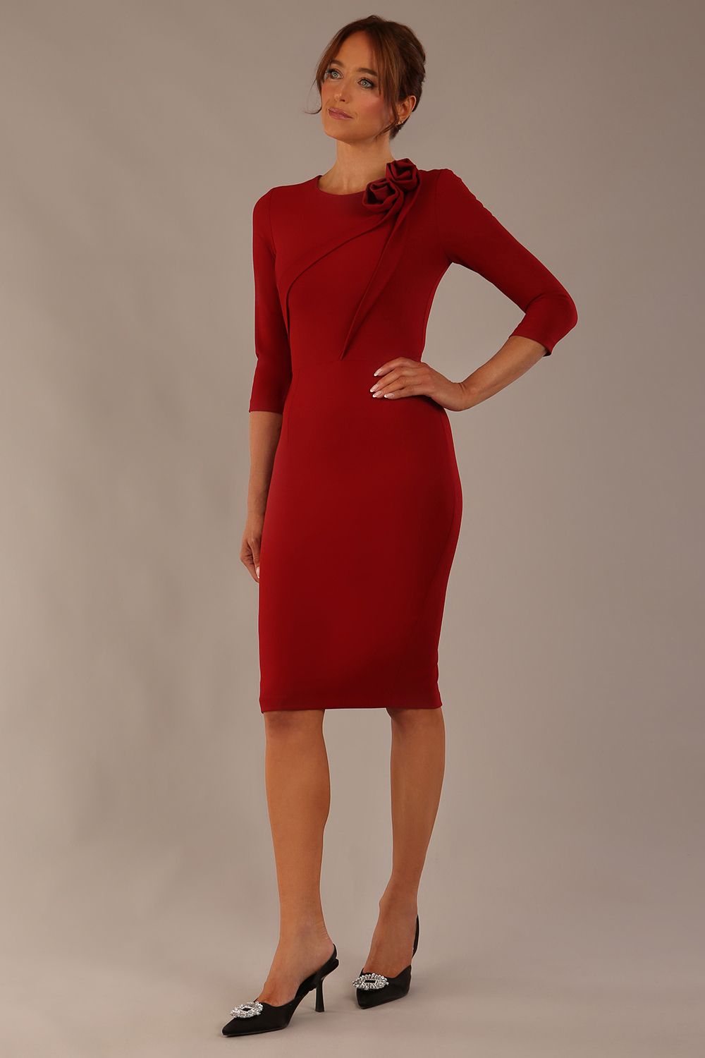 brunette model is wearing a diva catwalk Mirabelle ¾ Sleeves & Floral Shoulder Detail Pencil Dress with diagonal pleating across the front knee length in rosewood red colour front image