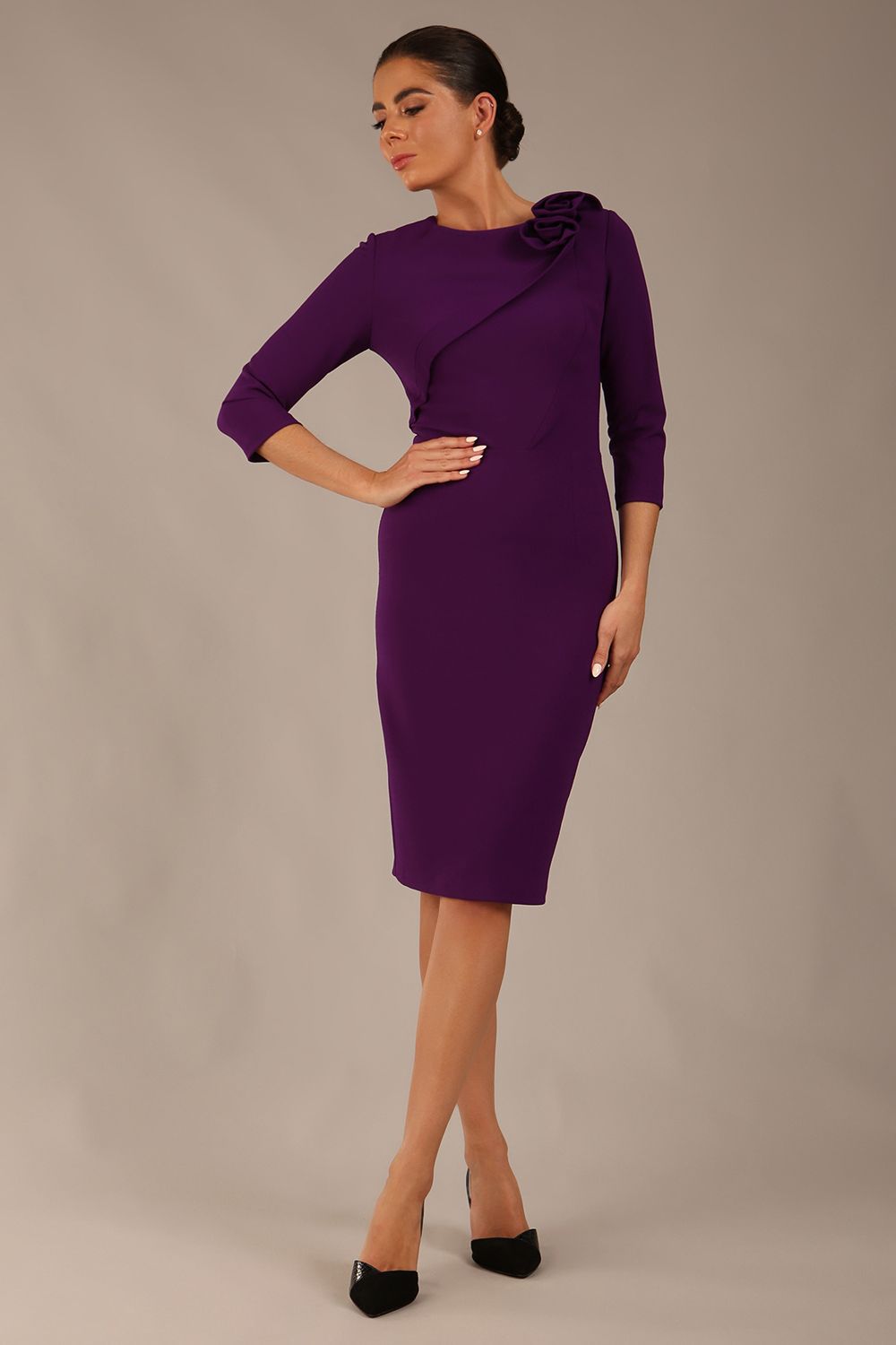 brunette model is wearing a diva catwalk Mirabelle ¾ Sleeves & Floral Shoulder Detail Pencil Dress with diagonal pleating across the front knee length in purple colour front image
