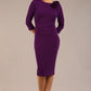 brunette model is wearing a diva catwalk Mirabelle ¾ Sleeves & Floral Shoulder Detail Pencil Dress with diagonal pleating across the front knee length in purple colour front image
