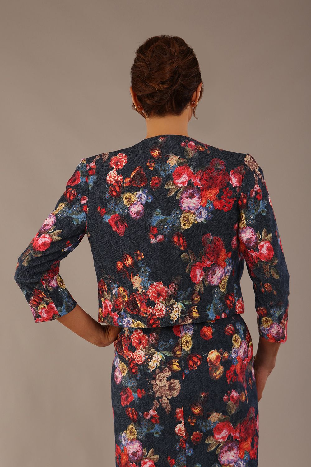 Back view of the Model wearing the Valetta cropped floral jacquard jacket over a matching dress with a plain background (Hidcote Floral)