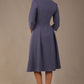 Model wearing the Ario pleated A-line dress in blue mineral, showcasing the round neckline and 3/4 sleeves, back view