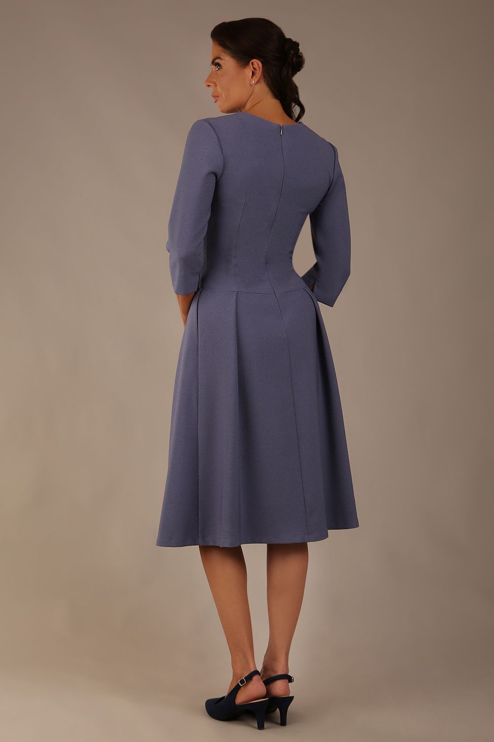 Model wearing the Ario pleated A-line dress in blue mineral, showcasing the round neckline and 3/4 sleeves, back view