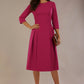 Model wearing the Ario pleated A-line dress in festive fuchsia, showcasing the round neckline and 3/4 sleeves