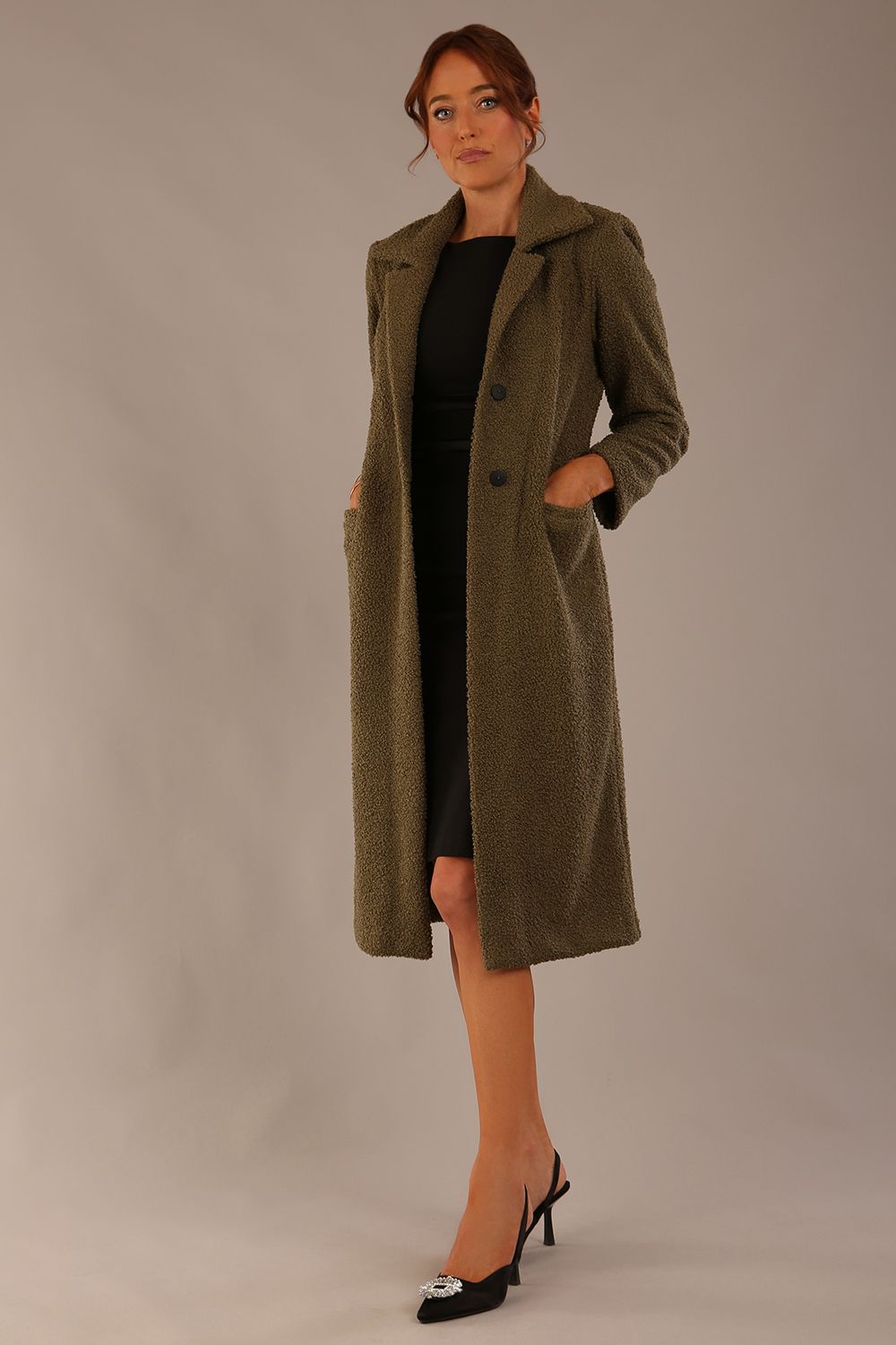 Woman wearing a long olive green Ambrose Boucle Midi Coat over a black Rialto sleeveless pencil dress on a plain background