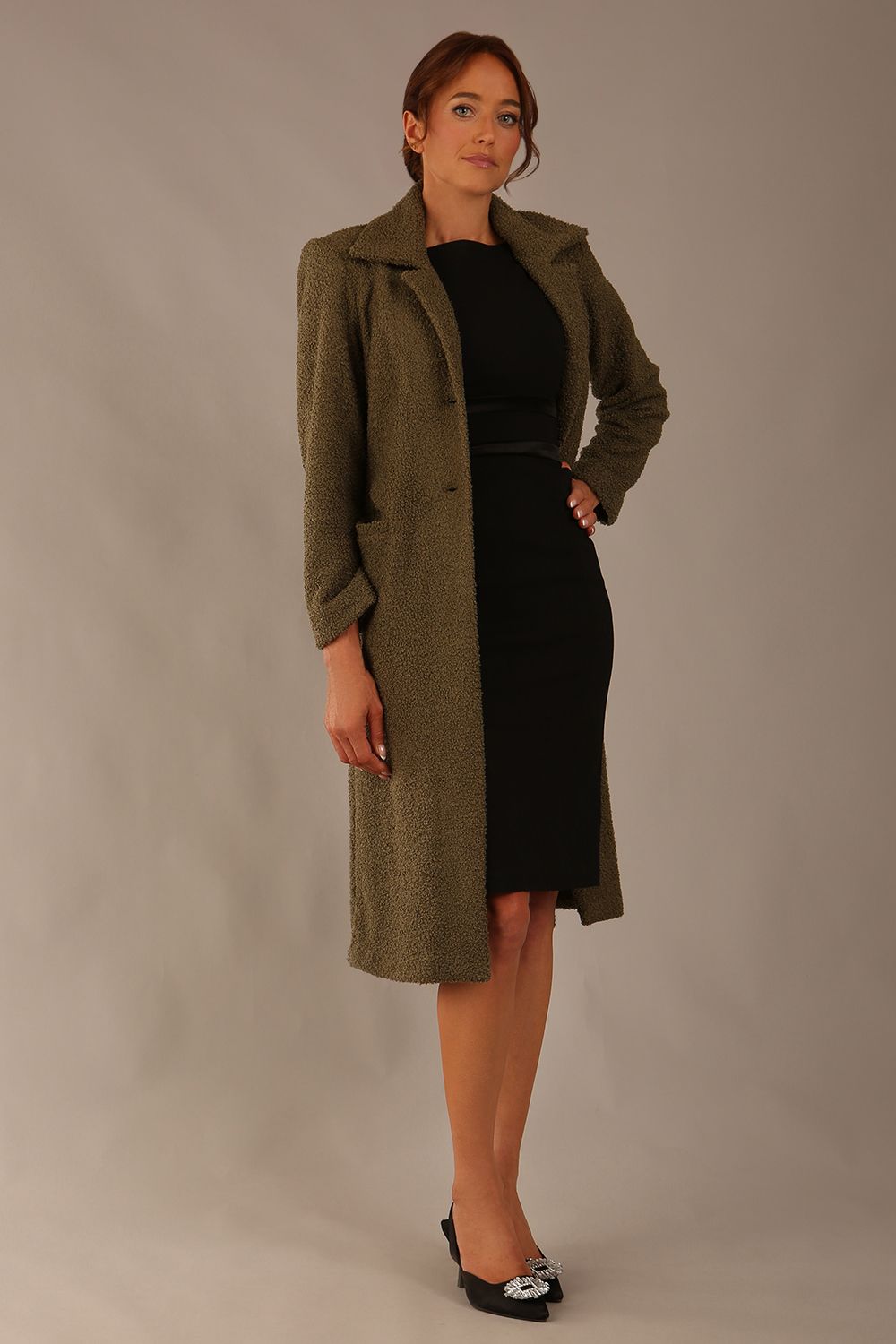 Woman wearing a long olive green Ambrose Boucle Midi Coat over a black Rialto sleeveless pencil dress on a plain background