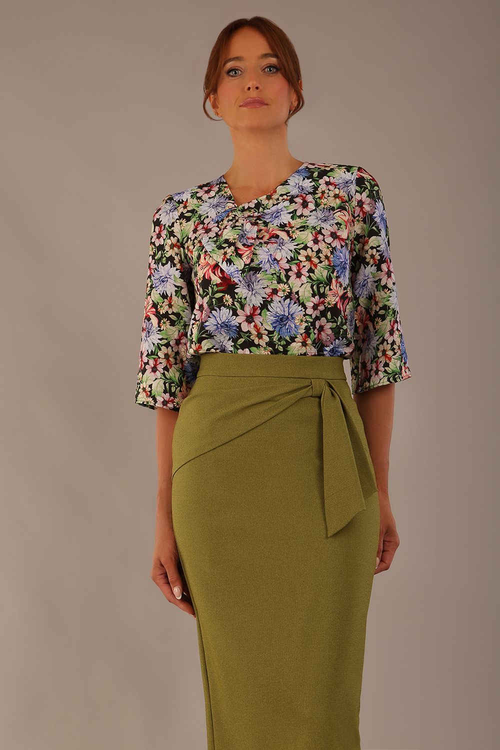 Model wearing a Suki asymmetric draped top in the Aurora Botanical print, styled with a olive green pencil skirt.