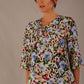 Model wearing a Suki asymmetric draped top in the Aurora Botanical print, styled with a black fishtail skirt.