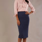 Woman wearing a pink blouse with a bow and a navy skirt on a plain background