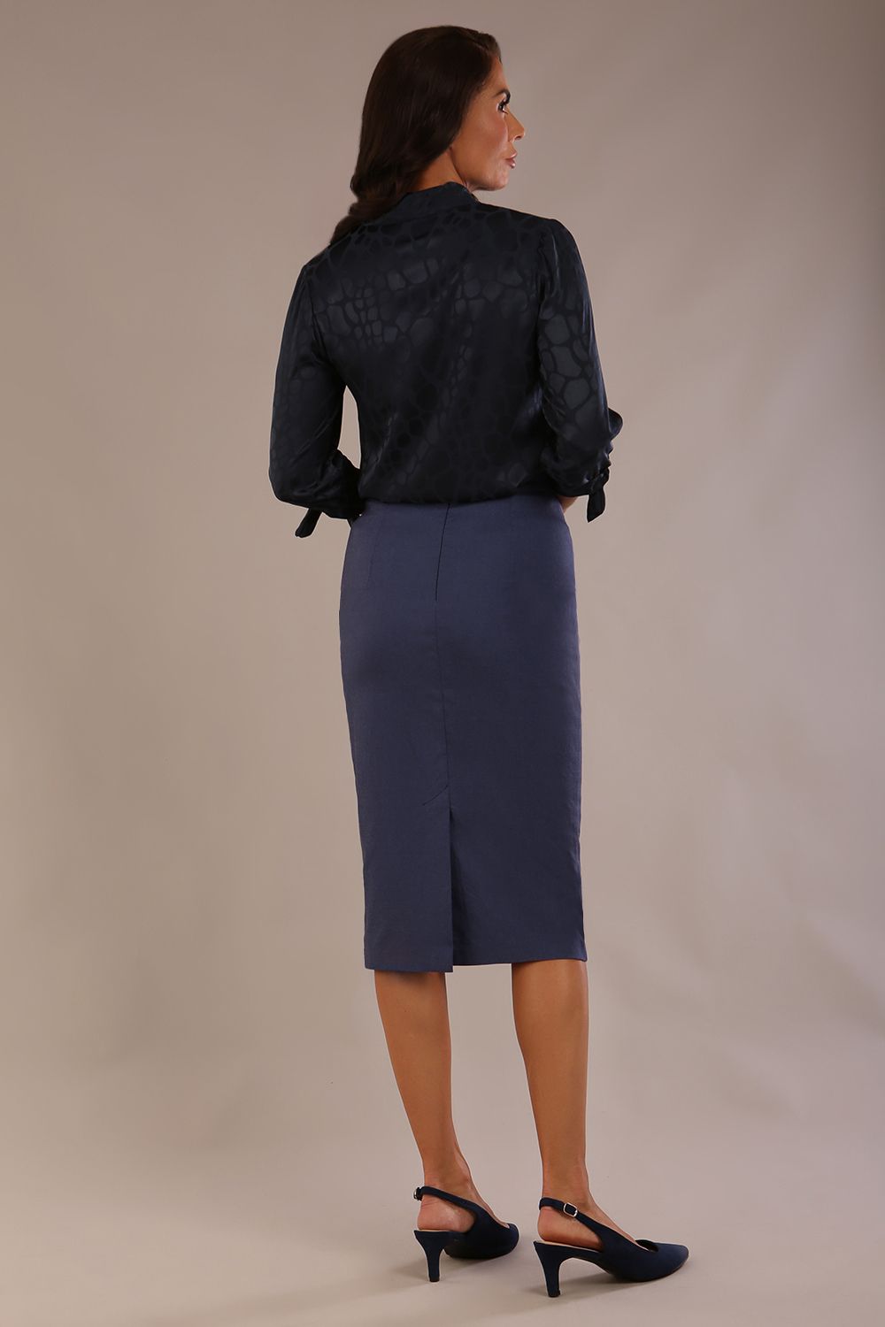 Model wearing a navy satin pebble top with a tie neckline and 3/4 sleeves, styled with a navy pencil skirt.