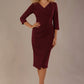 Woman wearing The Adley asymmetric draped pencil dress in rich burgundy red against a plain background